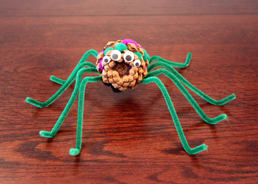 Decorated pine cone spider with googly eyes and purple pom poms